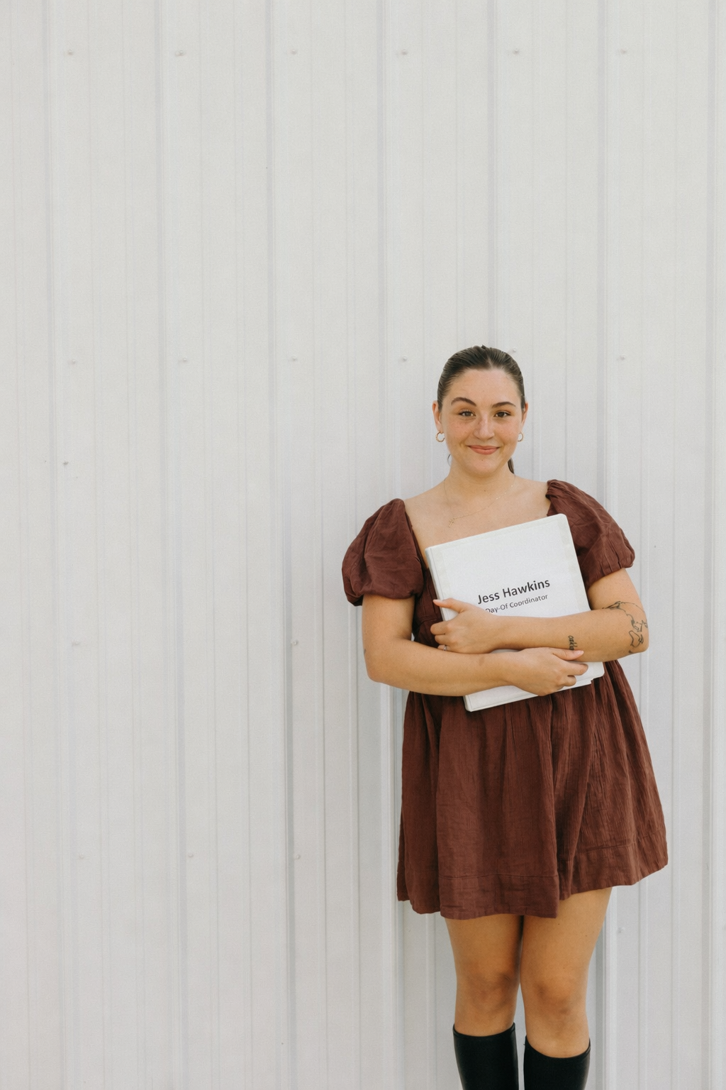 Jess Hawkins standing against a white wall holding a portfolio.